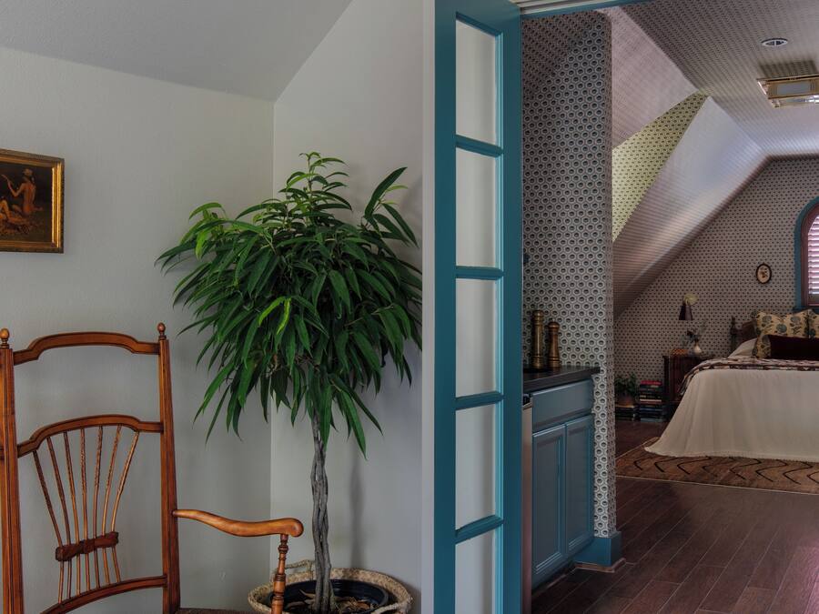 A room with a checkered floor, a wooden chair, a potted plant, and a blue door leading to another room.