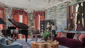 A spacious living room with a grand piano, a comfortable sofa, a coffee table, and a large painting on the wall. - The Menagerie (Fredericksburg)