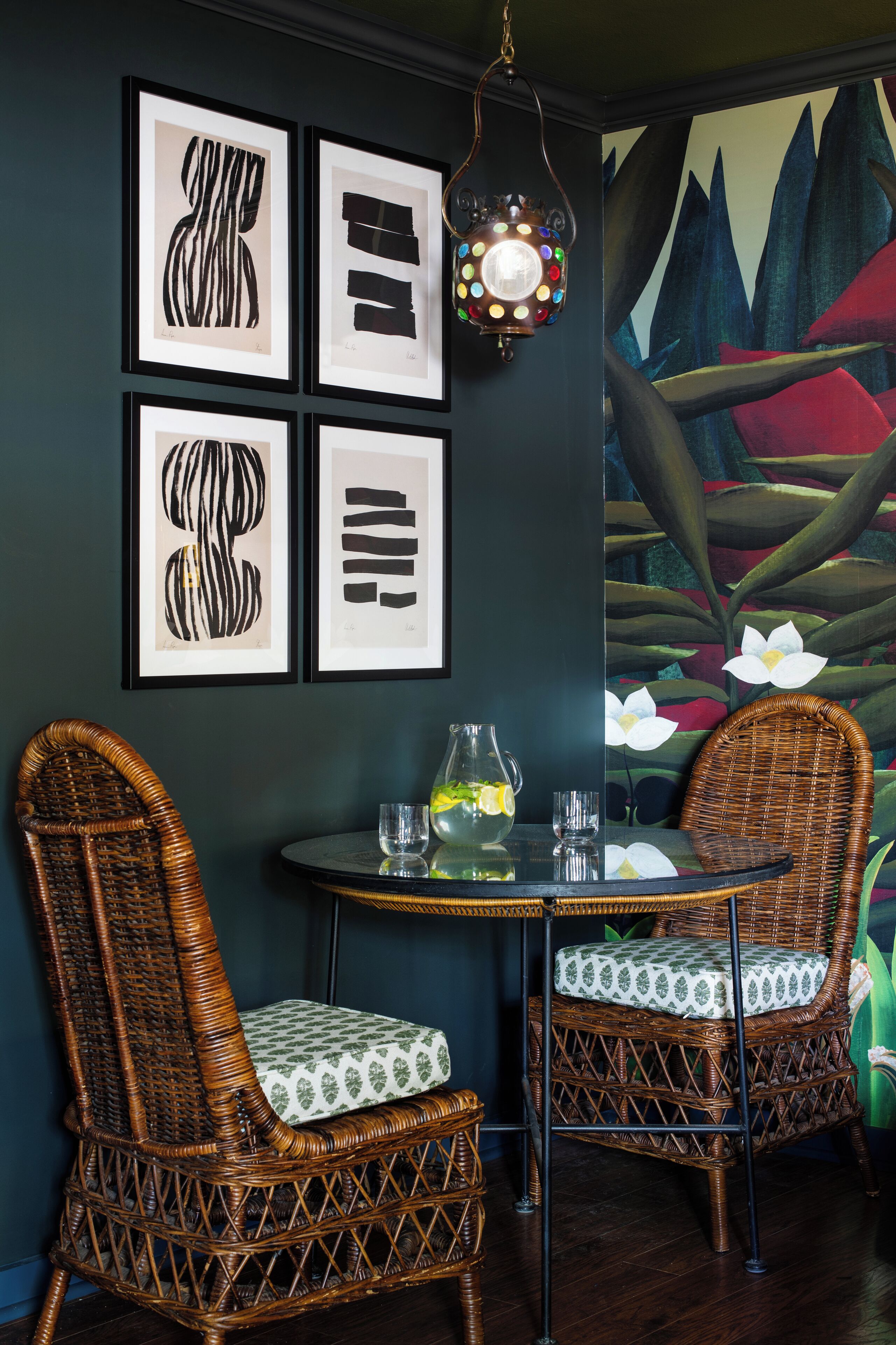 A room with two wicker chairs, a round table, and a wall with framed abstract art.