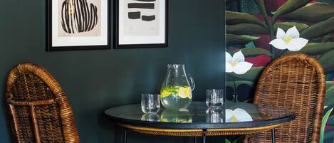 A room with two wicker chairs, a round table, and a wall with framed abstract art.