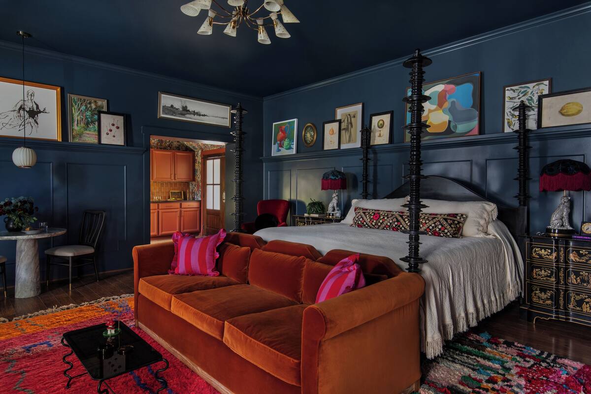 Une chambre à coucher avec un lit à baldaquin, un canapé rouge et divers tableaux encadrés accrochés aux murs.