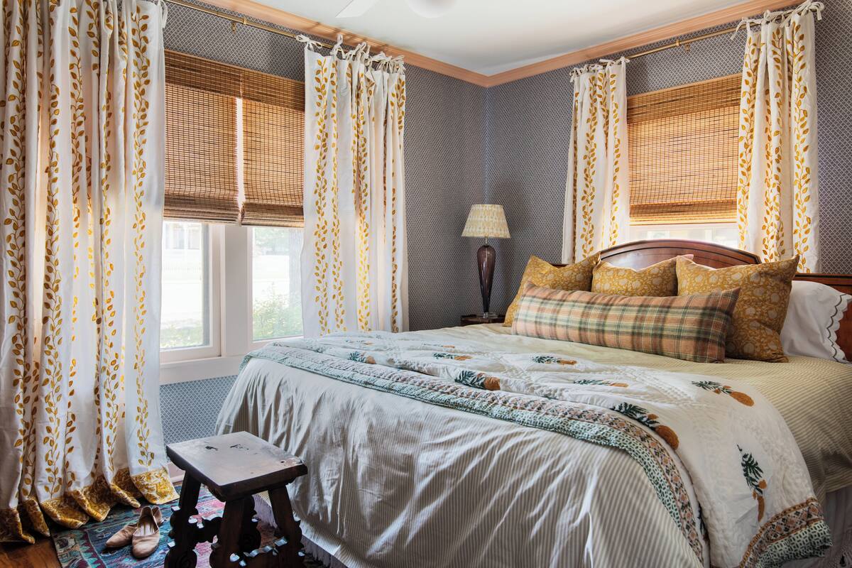 Une chambre à coucher avec un grand lit, une table de chevet, une lampe et des rideaux à motifs de feuilles.