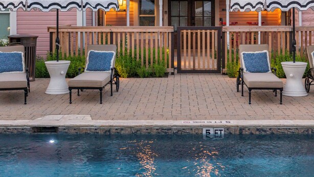 A two-story house with a balcony, a swimming pool, and outdoor seating with umbrellas. - The Menagerie (Fredericksburg)