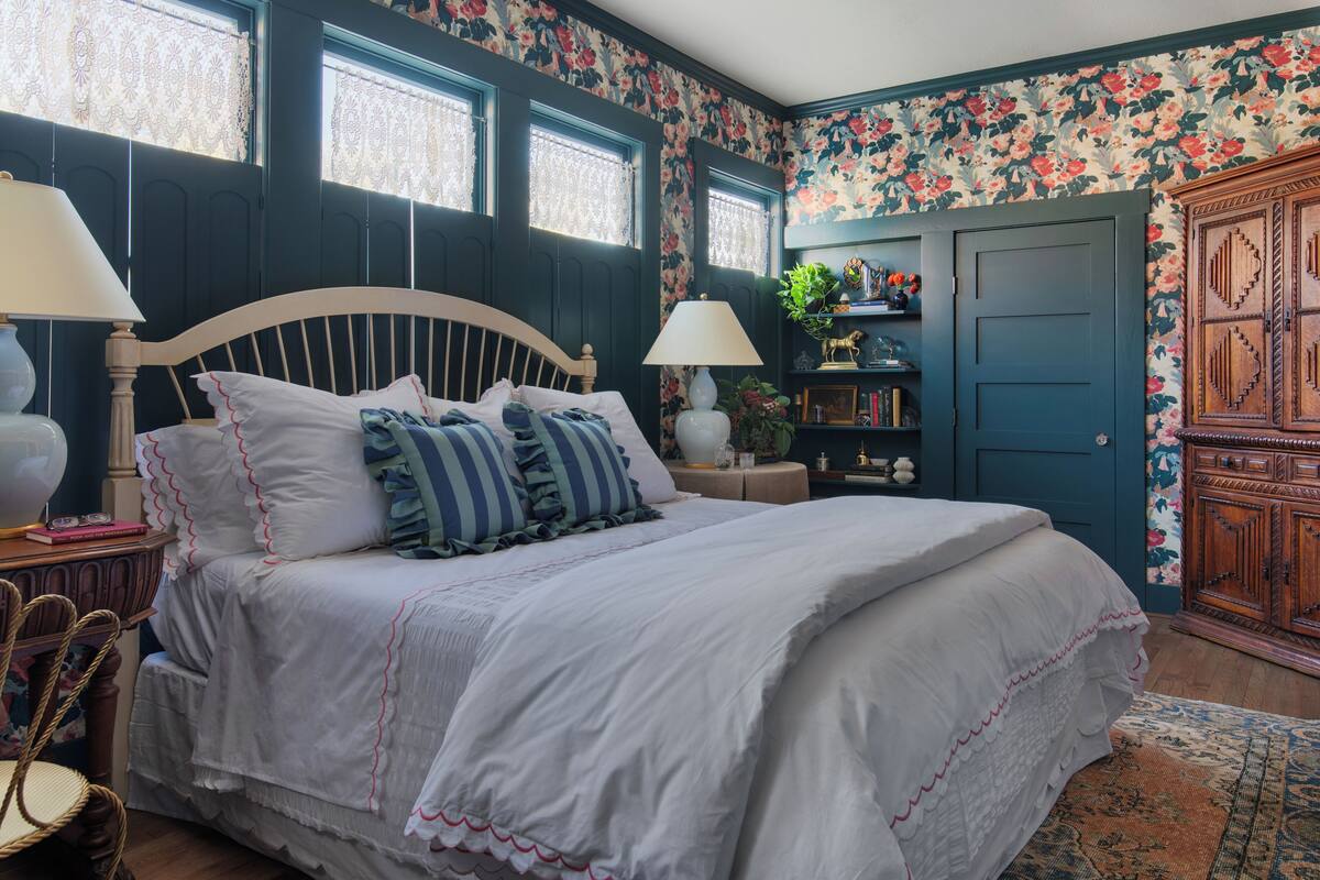 Une chambre à coucher avec un grand lit, deux lampes de chevet, une armoire en bois et un papier peint à motifs floraux.