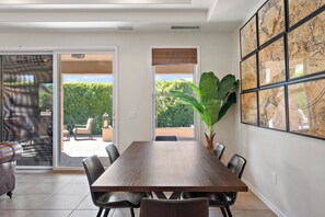 A dining area with a wooden table and chairs, large windows, and a view of greenery outside. - Chandler Keep – Medieval Spanish Villa, BBQ Courtyard & Prime South Chandler (Chandler)