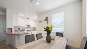 Una cocina moderna con armarios blancos, una isla de madera y un comedor con una mesa grande y sillas.