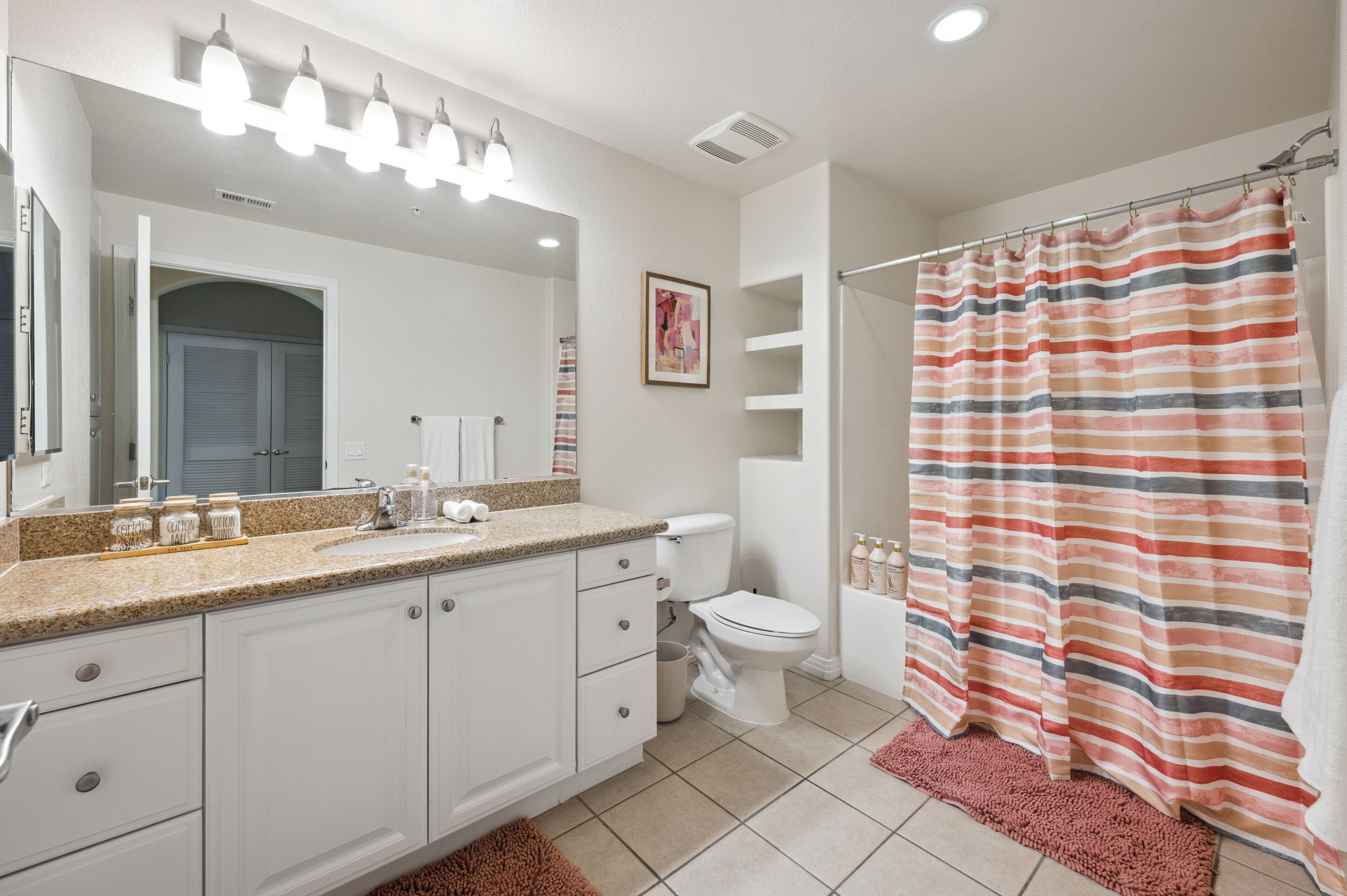 A bathroom with a white vanity, a toilet, a shower curtain, and a mirror with lights.