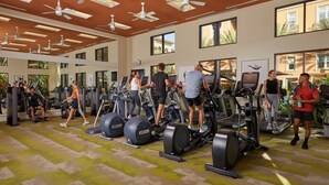 Un gimnasio con cintas de correr, bicicletas estáticas y ventiladores de techo.