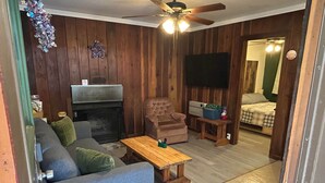 Ein Wohnzimmer mit Kamin, einer Couch, einem Couchtisch, einem Fernseher und einem Deckenventilator.