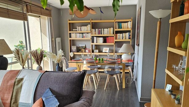 A living room with a dark wood floor, a grey sofa with cushions, a dining table with chairs, and a bookshelf filled with books. - Quiet 2B/1B Downtown Condo, Hills View, Bright, Spacious, Recently Remodeled (Aurillac)