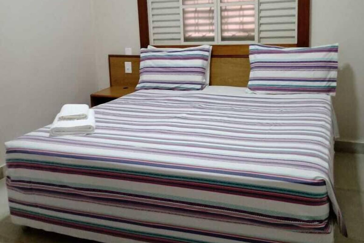 A bed with a striped bedspread, two pillows, a nightstand, and a wall-mounted air conditioner.