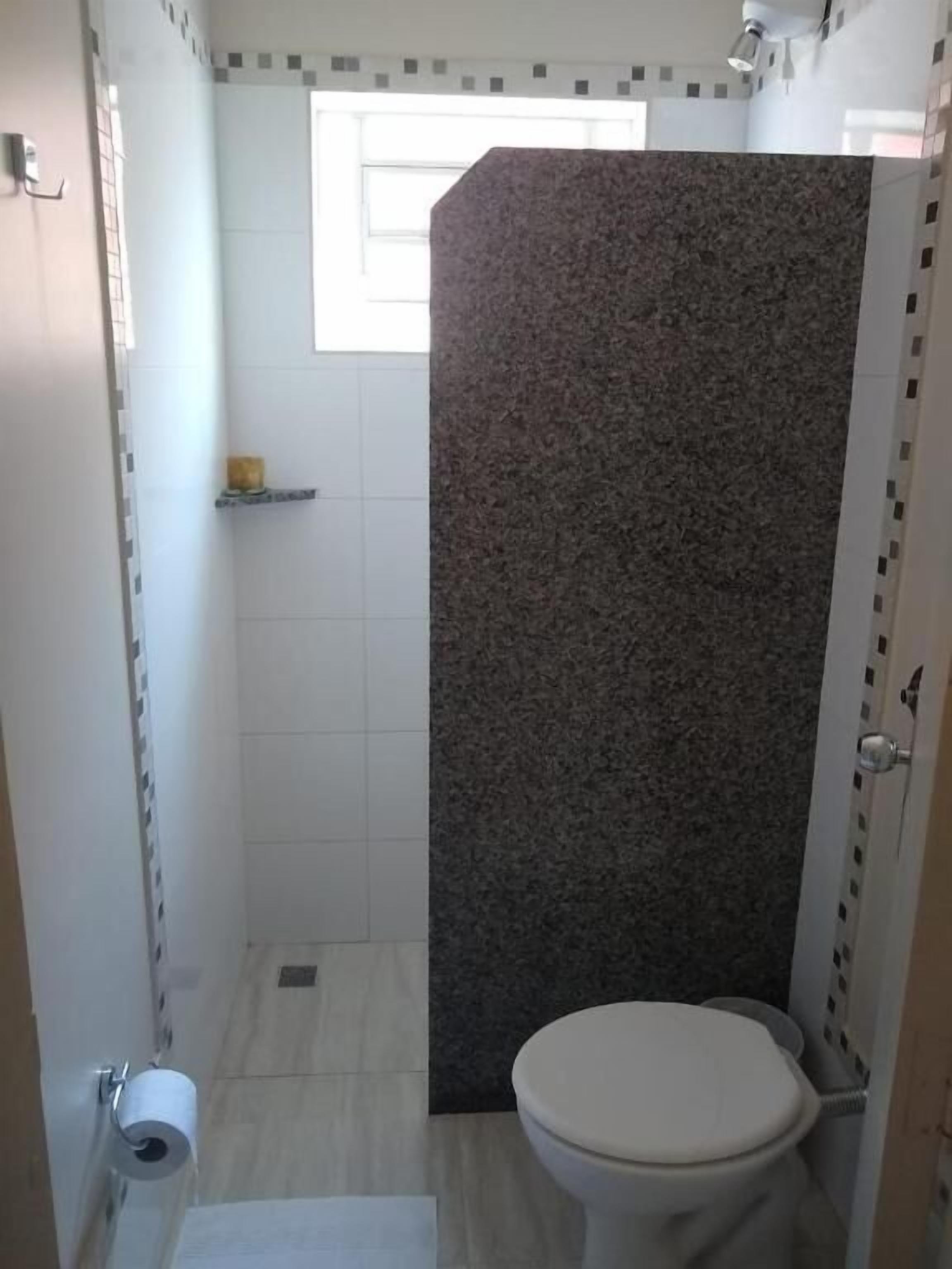 A small bathroom with a toilet, a shower enclosure, and a tiled floor.