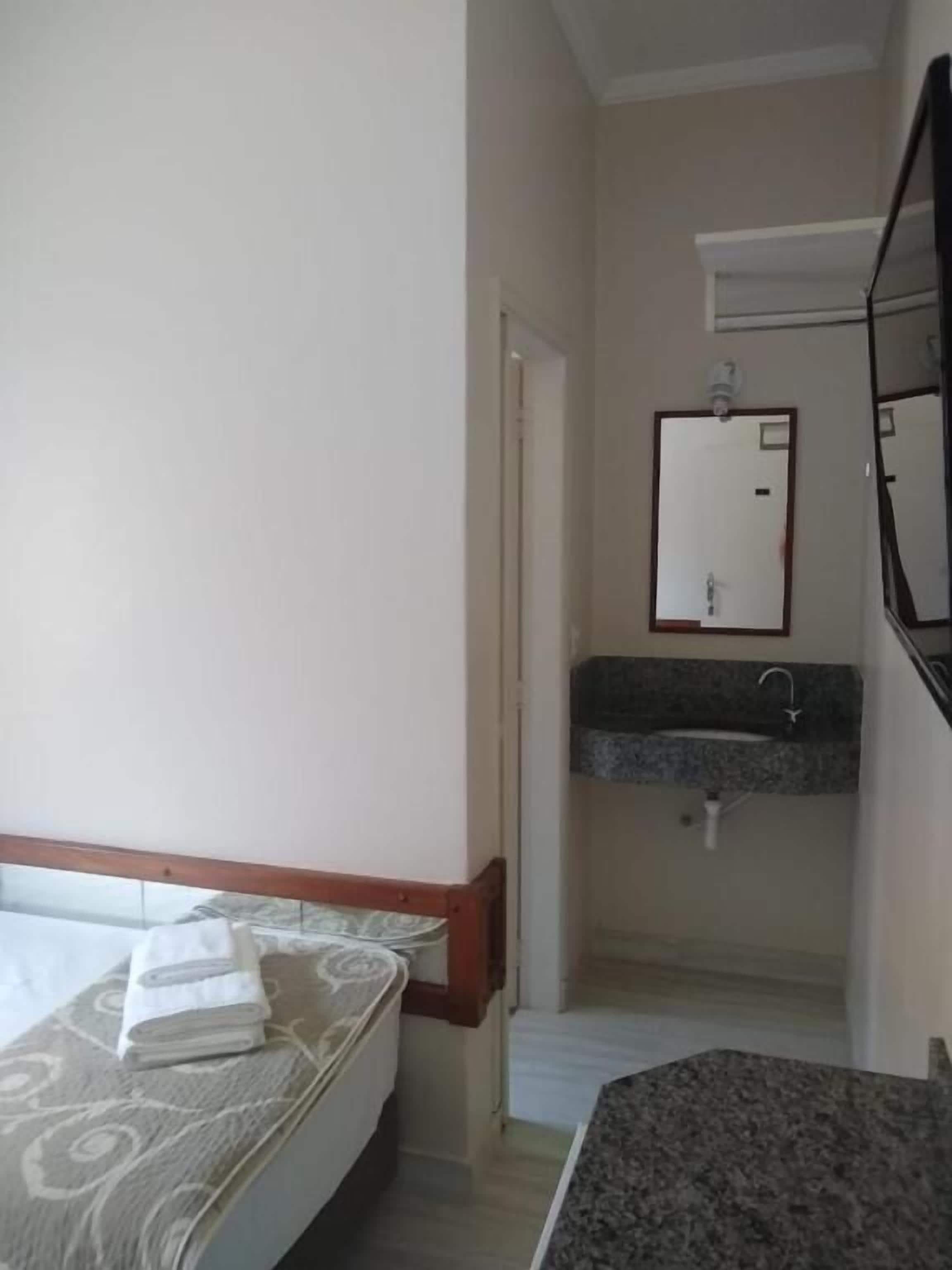 A bedroom with a bed, a bathroom with a sink and mirror, and a small hallway.