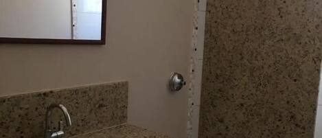 A bathroom with a granite countertop sink, a toilet, and a shower area.