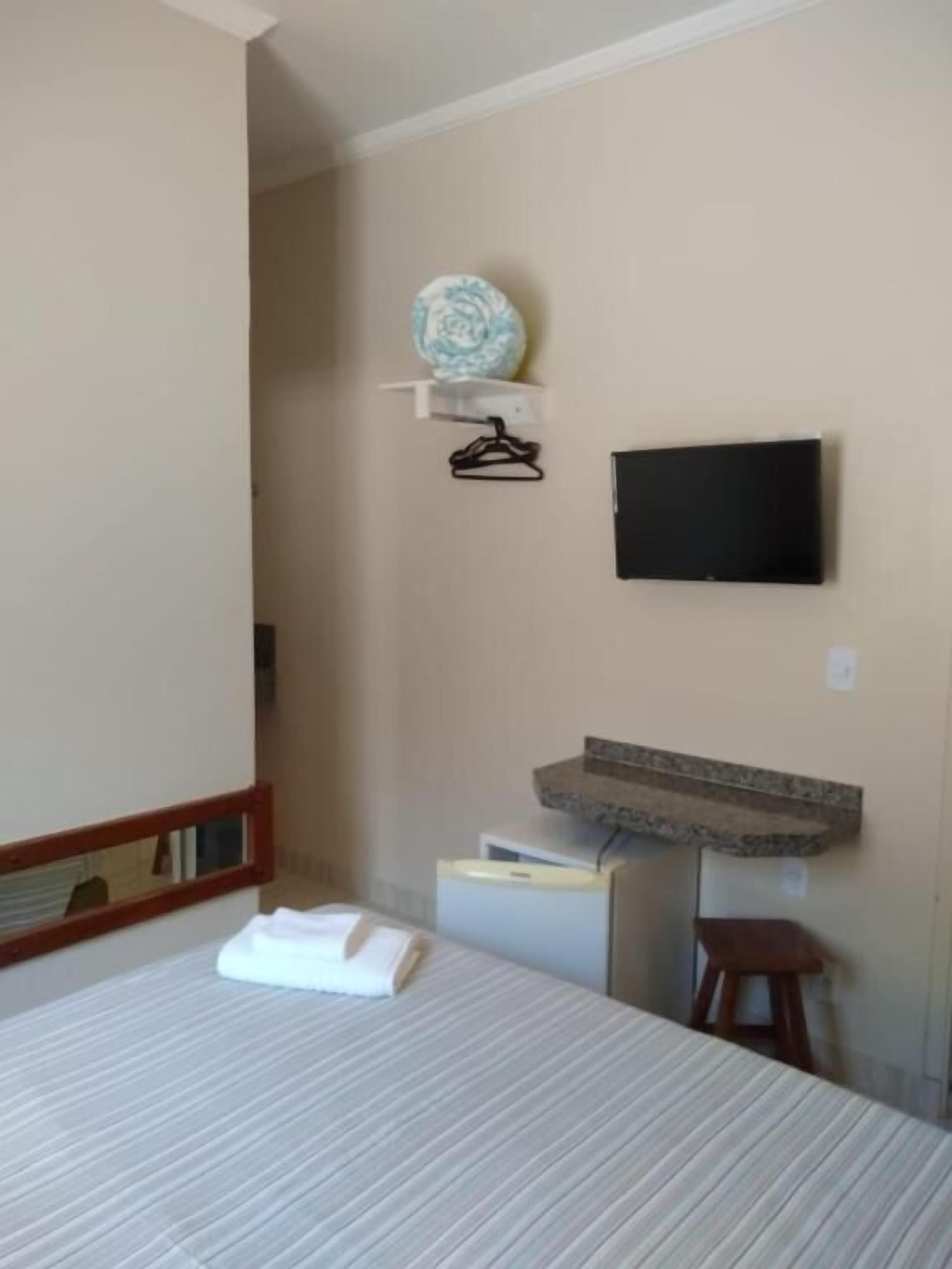 A hotel room with a bed, a flat-screen TV mounted on the wall, a small shelf with a decorative item, and a mirror.