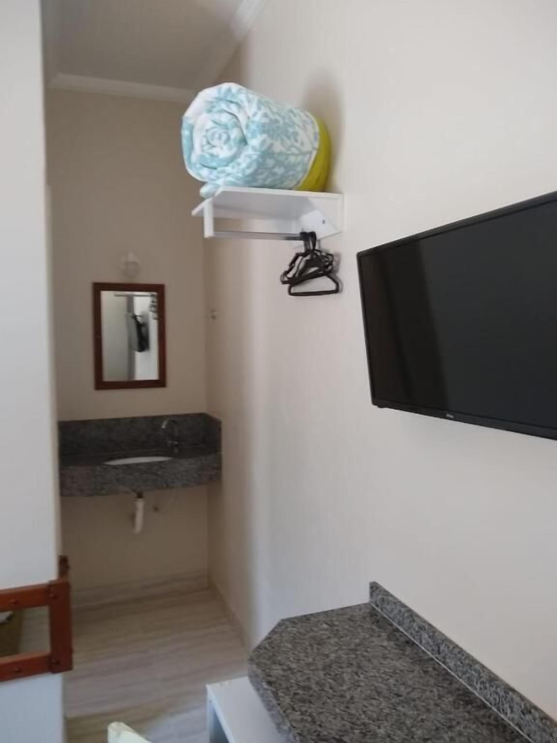 A bathroom with a granite countertop sink, a mirror, a towel rack, and a mounted television.