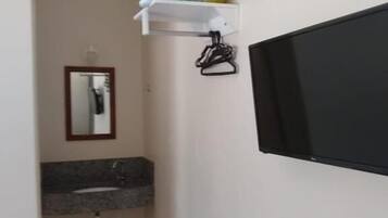 A bathroom with a granite countertop sink, a mirror, a towel rack, and a mounted television.