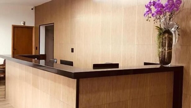 Una zona de recepción con un mostrador de madera, un florero con flores moradas y suelo de madera.