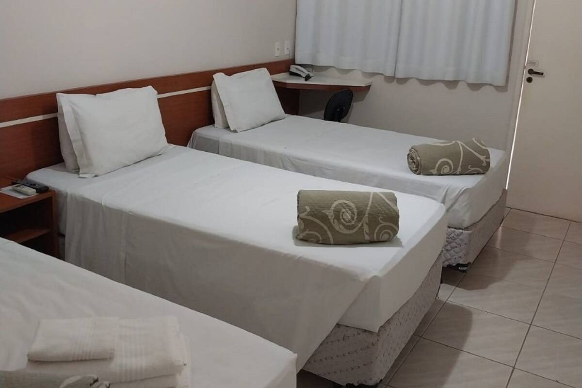 A hotel room with two beds, a desk, an air conditioning unit, and a door.