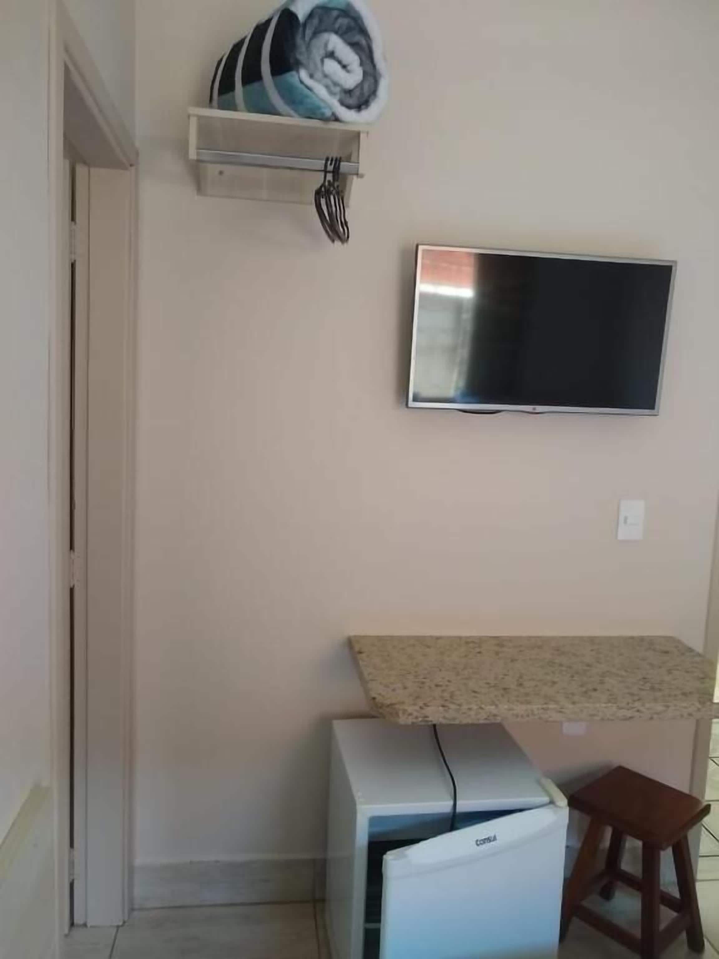 Una pequeña kitchenette con refrigerador, microondas y una encimera. Hay un televisor montado en la pared sobre la encimera.