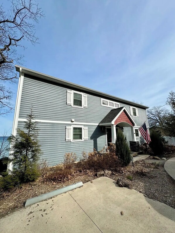 A two-story house with a red roof, white shutters, and an American flag.