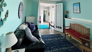 A living room with a blue wall, a wooden bench, a black leather sofa, a blue patterned rug, a ceiling fan, and a clock on the wall. - The Place Up North (Traverse City)