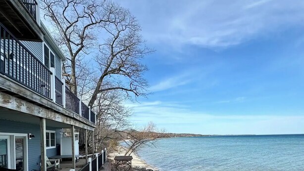 A waterfront property with a covered deck, stone steps leading to a dock, and a view of the water. - The Place Up North (Traverse City)
