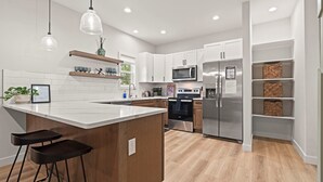 Een moderne keuken met witte kasten, roestvrijstalen apparatuur en een centraal keukenblok met barstoelen.