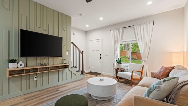 Een moderne woonkamer met een flatscreen televisie aan de muur, een ronde salontafel, een bank en een trap naar een andere kamer.
