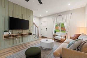 A modern living room with a flat-screen TV mounted on a wall, a round coffee table, a sofa, and a staircase leading to another room.