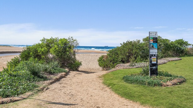 A pathway leading to a beach with a signpost in the foreground. - Coastal retreat near shops + beach (Corrimal)