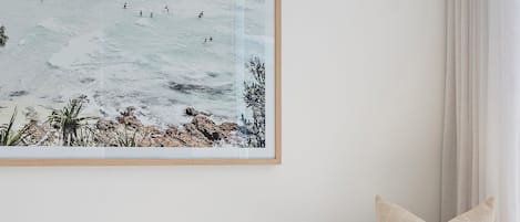 A room with a wicker chair, a framed artwork of a beach scene, and a woven rug.