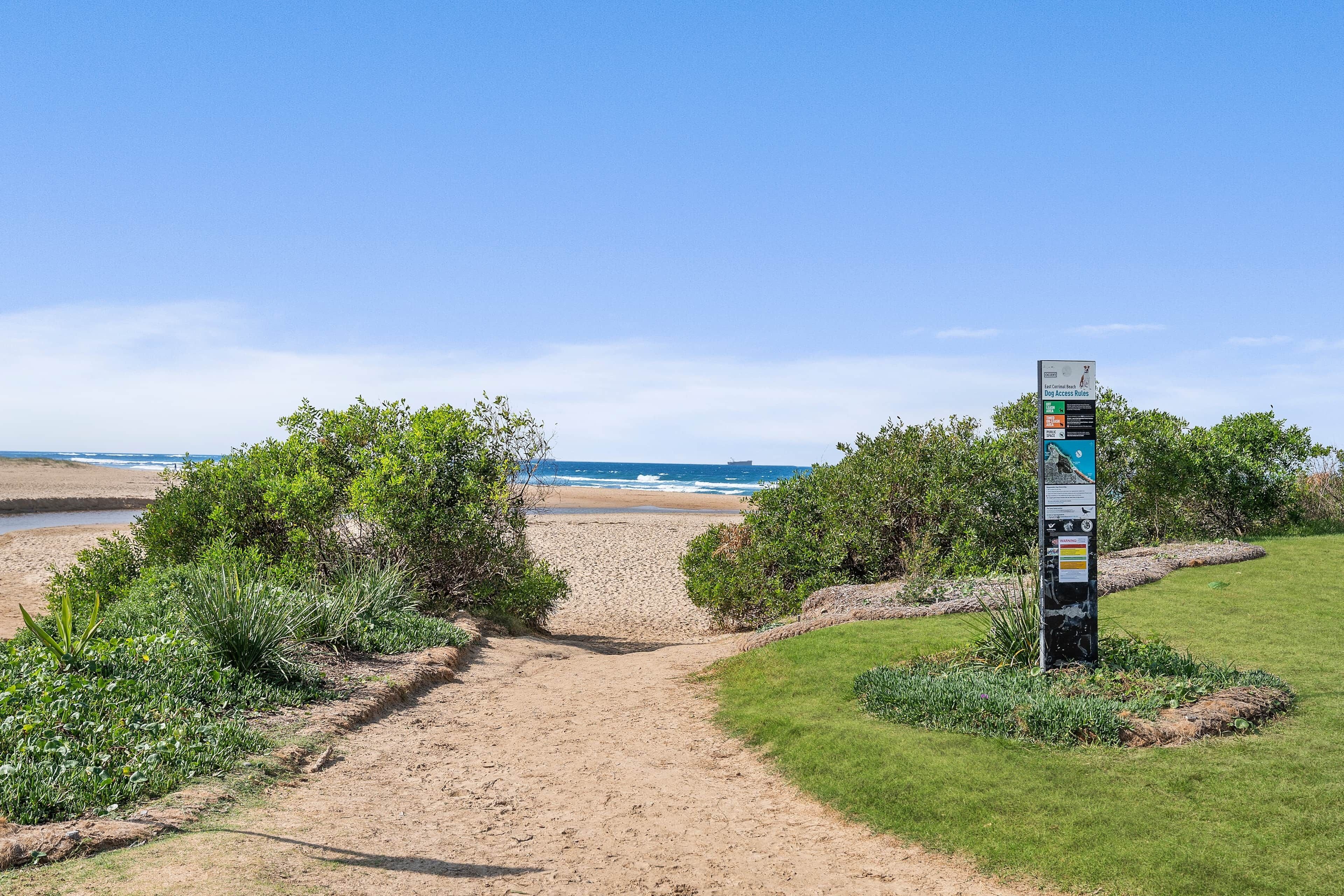 A pathway leading to a beach with a signpost in the foreground.