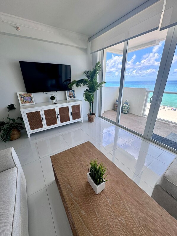 A modern living room with a large flat-screen TV, a white cabinet with wicker doors, a wooden coffee table, and a potted plant.
