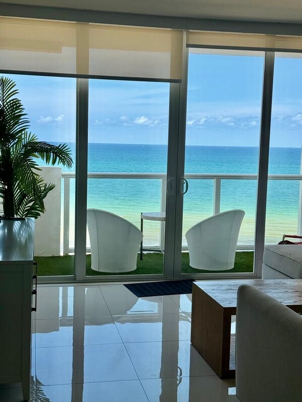 A modern living room with a large sliding glass door leading to a balcony with a view of the ocean.