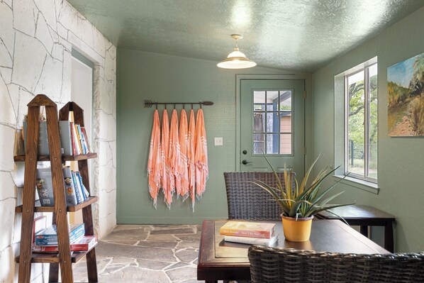 Un rincón acogedor para leer con una estantería, una mesa con libros, una planta en maceta y vistas al exterior.
