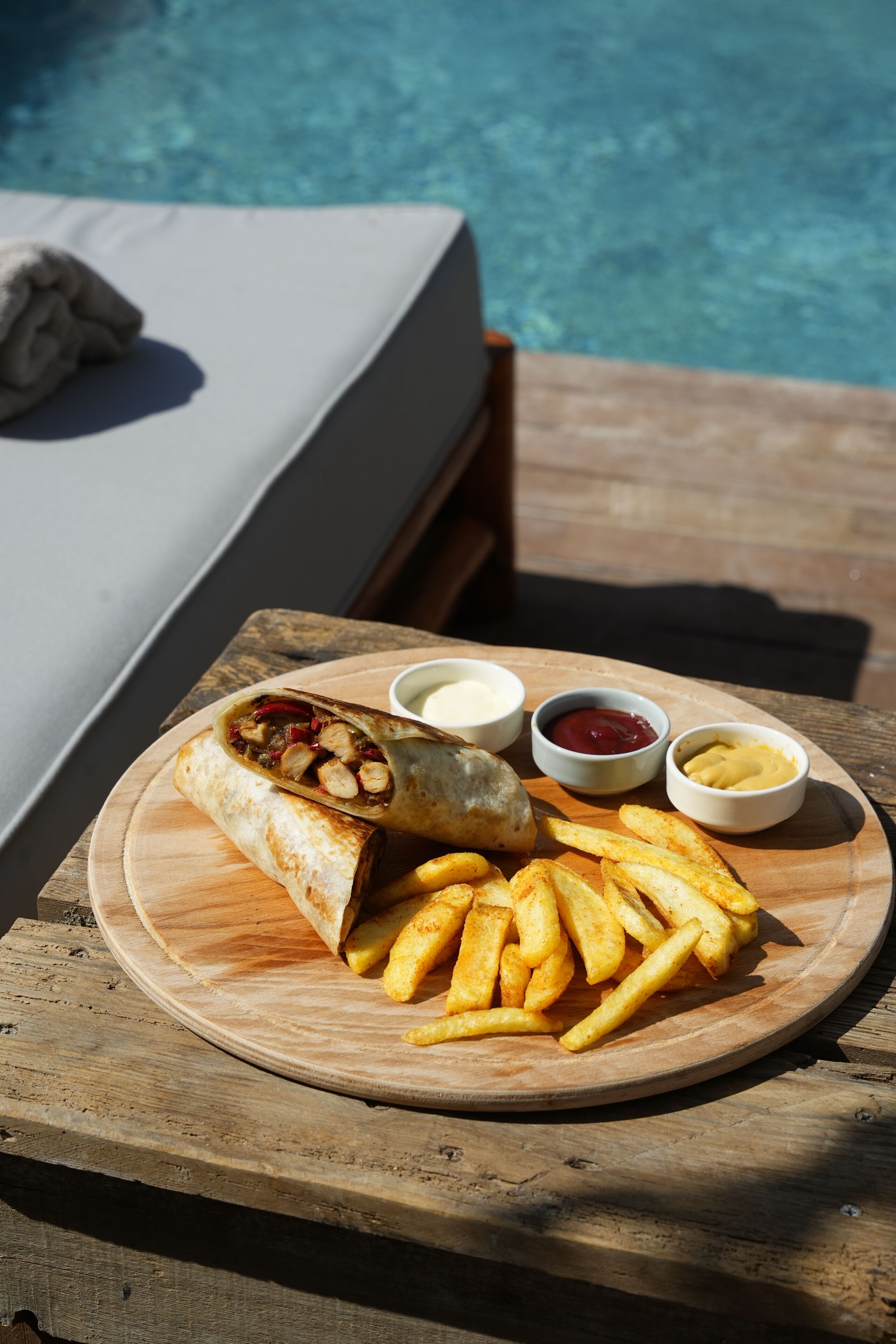 Una mesa de madera con un plato de comida, que incluye un wrap, papas fritas y tres salsas para mojar.