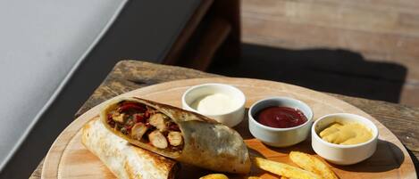 Una mesa de madera con un plato de comida, que incluye un wrap, papas fritas y tres salsas para mojar.