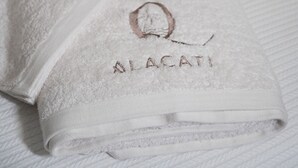 A neatly folded white towel with embroidered text on a bed. - Q Alacati Otel (Cesme)