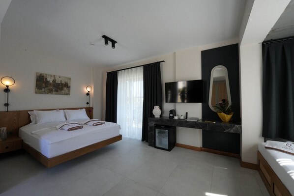 A modern hotel room with a large bed, a desk with a mirror, and a small refrigerator. - Q Alacati Otel (Cesme)