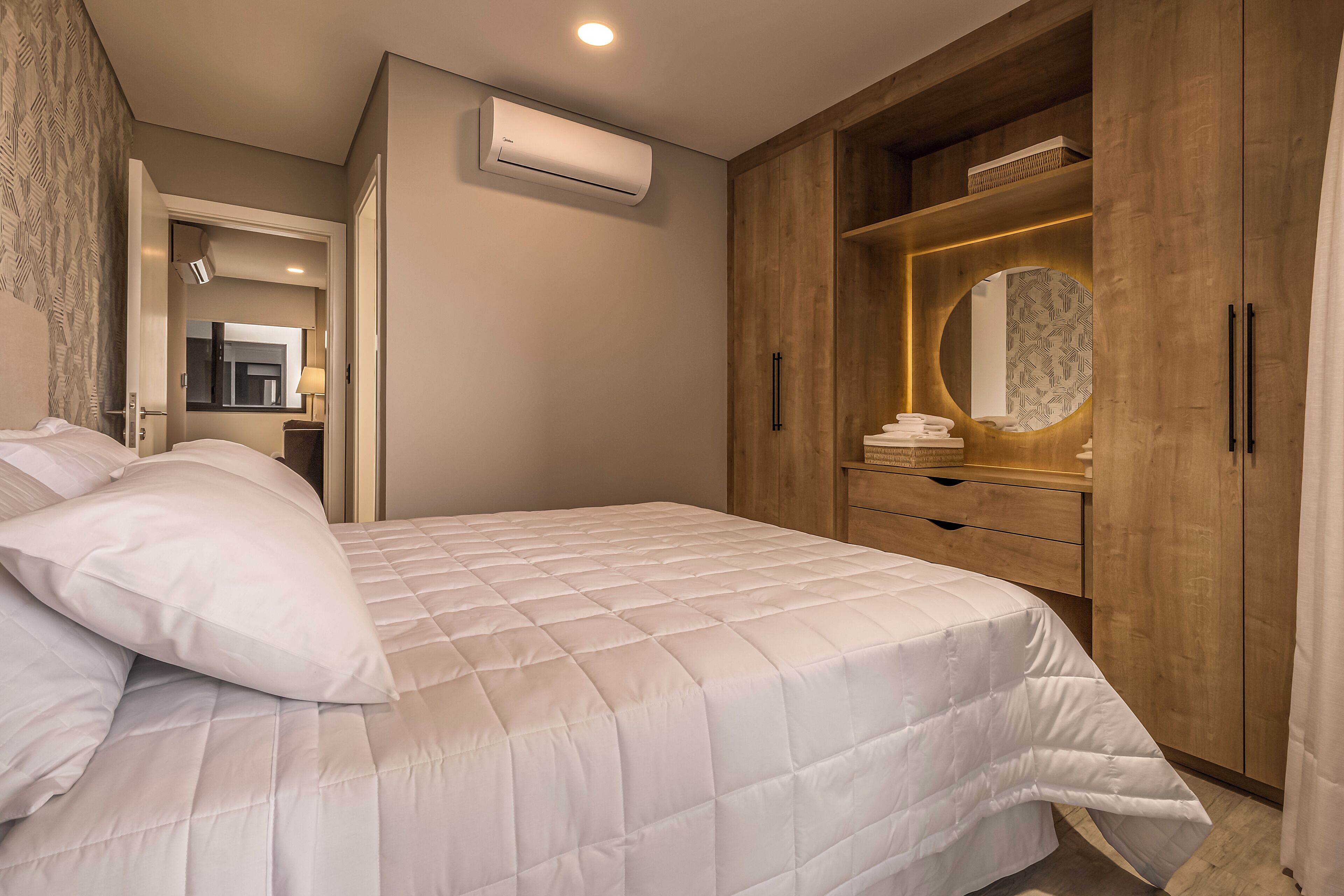 A bedroom with a large bed, a wooden wardrobe, a mirror, and an air conditioning unit.