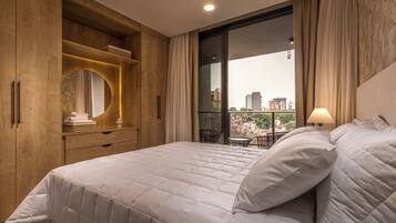 A bedroom with a large bed, wooden wardrobe, and a view of the city through a large window.