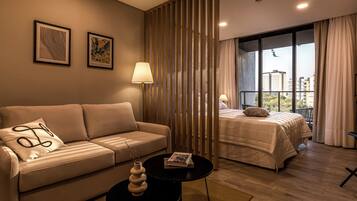 A modern hotel room with a sofa, a small table with a vase, a bed with a view of the city, and a decorative partition.