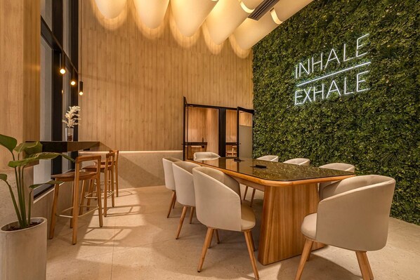 Una sala de reuniones moderna con una mesa de madera, sillas blancas y una pared verde con el texto 'INHALE EXHALE'.
