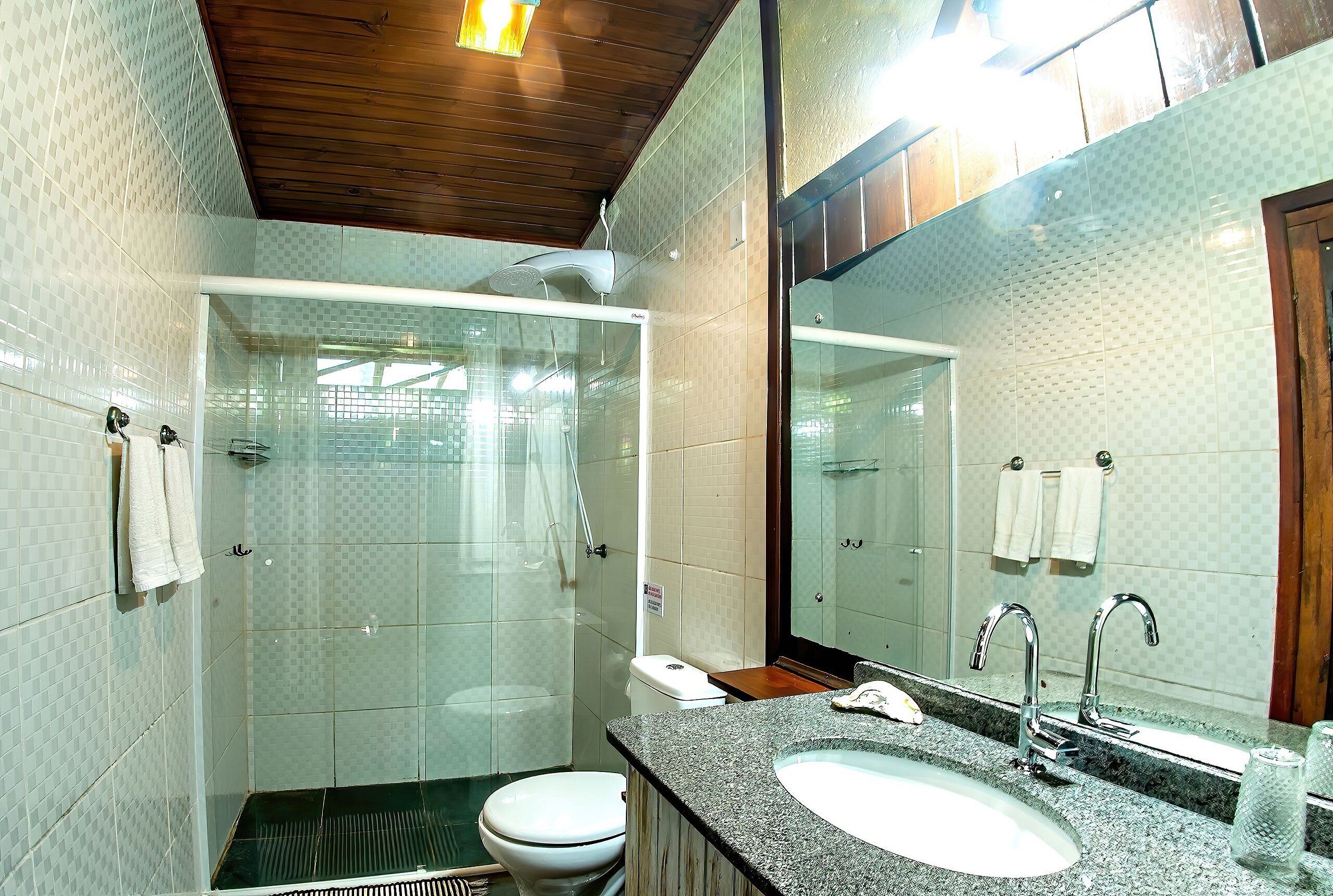 A bathroom with a glass-enclosed shower, a toilet, a sink with a mirror, and towels hanging on the wall.