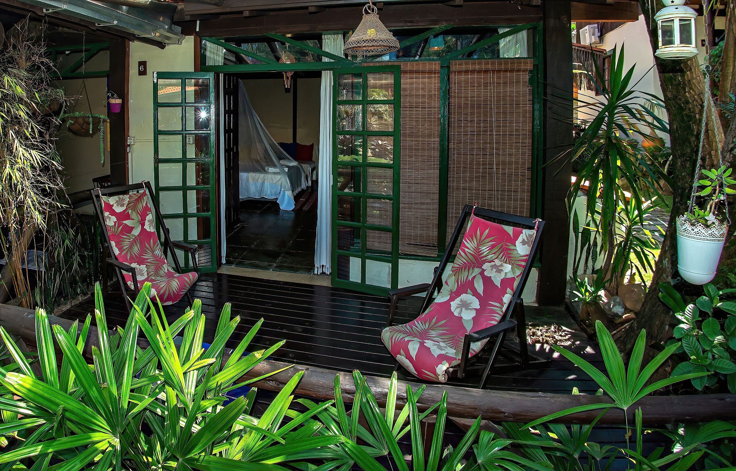 A tropical resort with a covered outdoor seating area, a wooden deck, and lush greenery.
