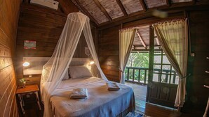 A wooden cabin bedroom with a canopy bed, a small bedside table, and a view of the outdoors through a door. - Pousada Rosa da Praia - Praia do Rosa (Imbituba)