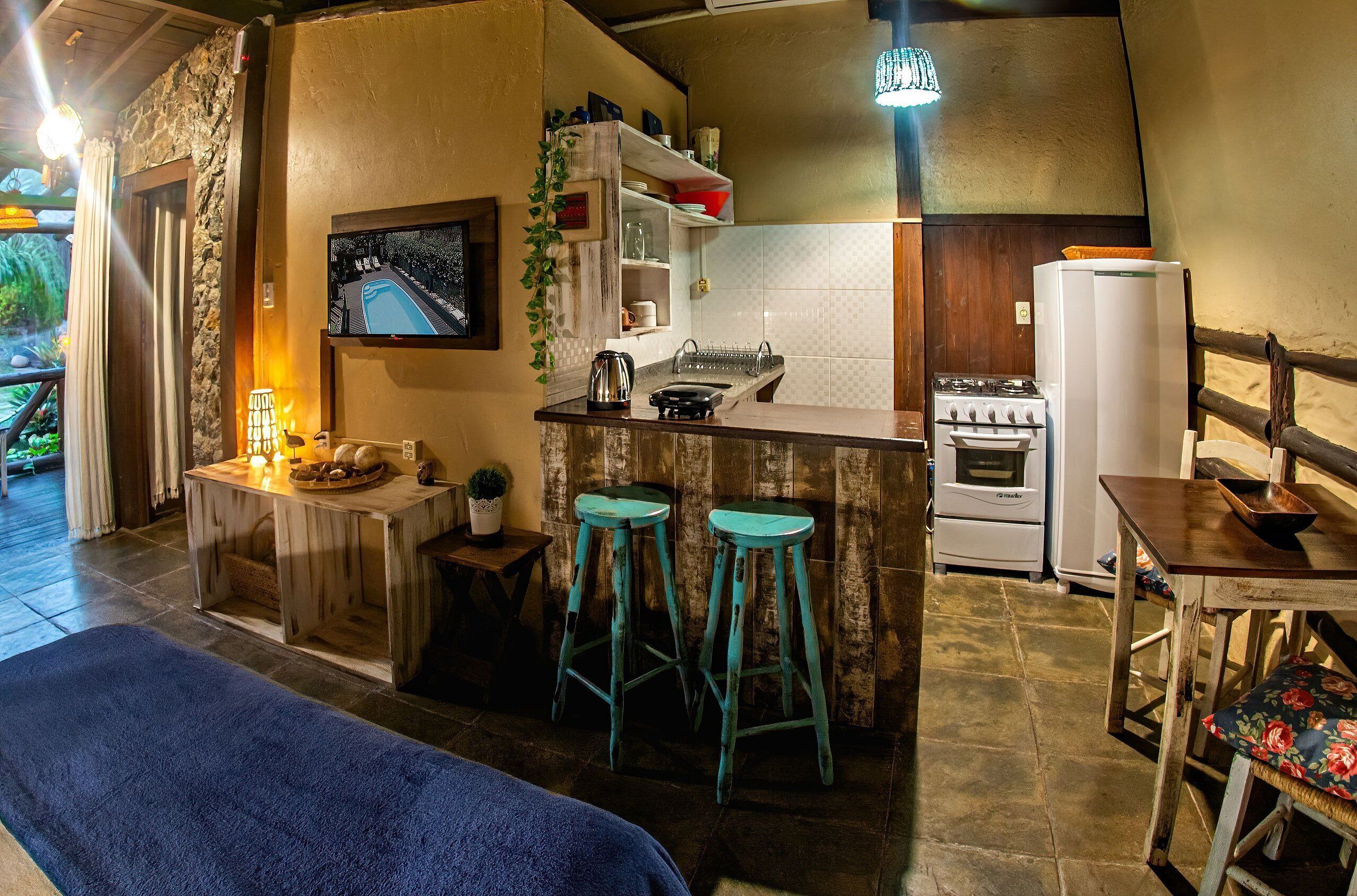 A compact kitchen with a stone wall, a small bar area with stools, a stove, and a refrigerator.