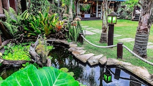 A serene garden with a pond, lush greenery, and a traditional building with a tiled roof. - Pousada Rosa da Praia - Praia do Rosa (Imbituba)