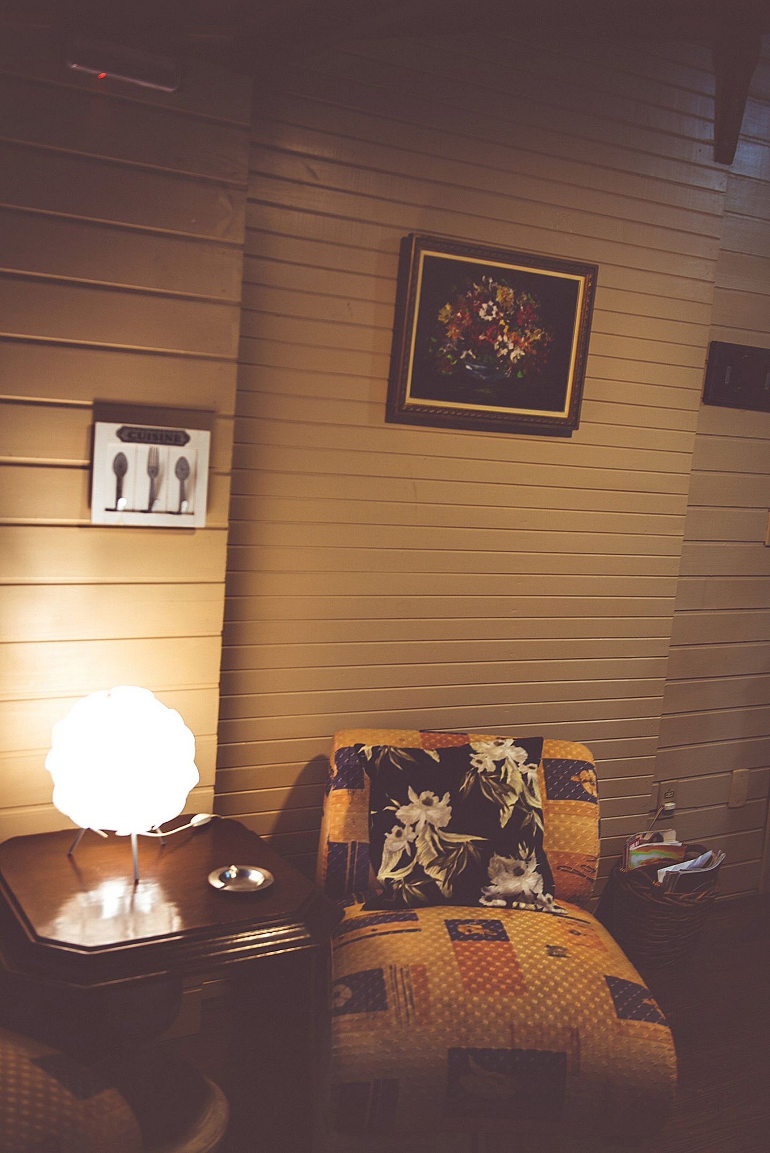 Una habitación acogedora con una pared de madera, un cuadro floral enmarco, una lámpara y un sofá estampado.